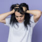 disappointed young brunette caucasian girl holds head looks down isolated purple wall 85x85